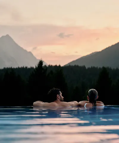Couple relaxing in an outdoor infinity pool with mountain views at sunset